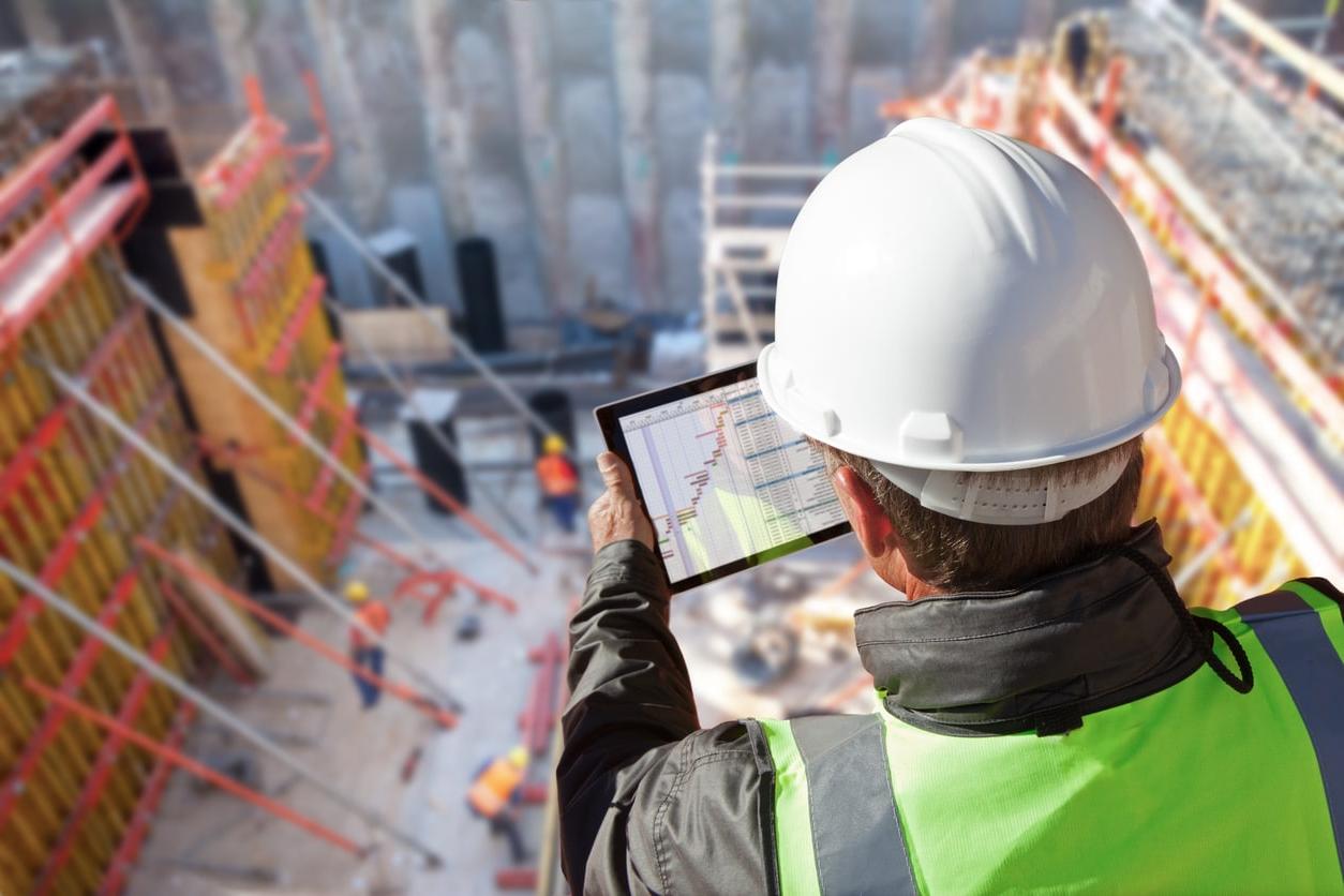 An engineer with a tablet looks down on a multi-level commercial construction site.